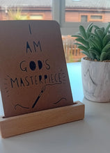 Load image into Gallery viewer, Brown sign with &#39;I AM GOD&#39;S MASTERPIECE&#39; text on a wooden stand, next to a potted plant.